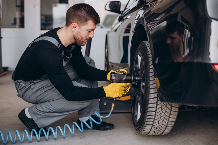 A mechanic in gloves uses a power tool to tighten the lug nuts on a car tire at a tyre shop in Singapore.