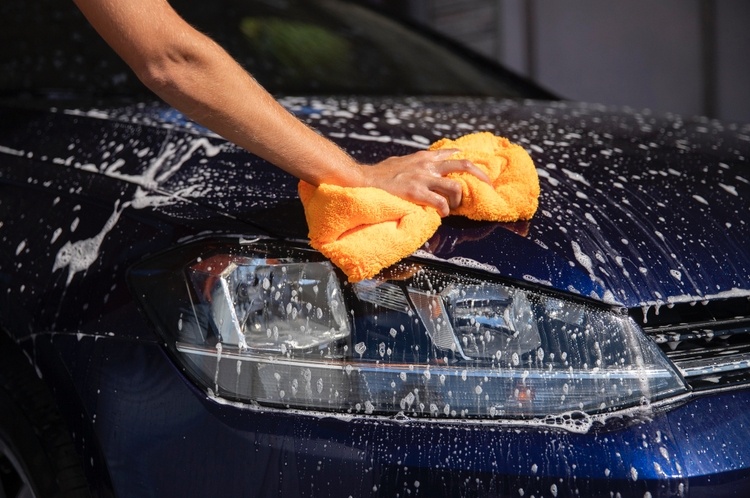 A person is washing the hood of a dark blue car with soapy water using an orange microfiber cloth, reflecting their dedication to car maintenance in Singapore.