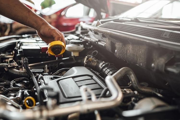 A person adds oil to a car engine in an open hood, ensuring that regular car maintenance Singapore recommends, like car air con servicing and other essentials, are up to date.