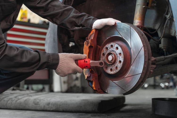 A mechanic wearing gloves uses a ratchet wrench to work on a brake disc and caliper assembly inside a garage, showcasing the meticulous car maintenance Singapore is known for.